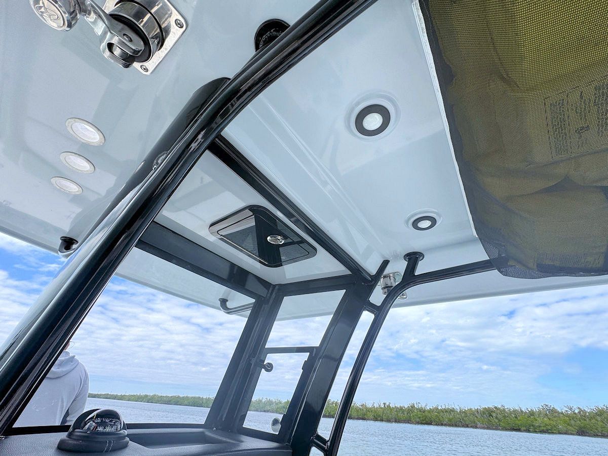 Interior view of a boat's white roof with black supports, spotlights, and black mesh shading. A person is visible in the distance.