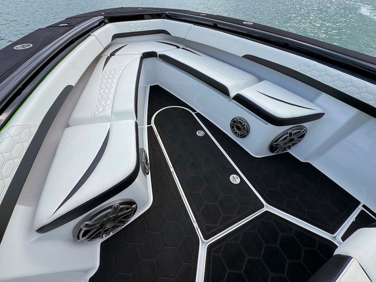 Boat interior with white seating and black flooring, featuring speakers.
