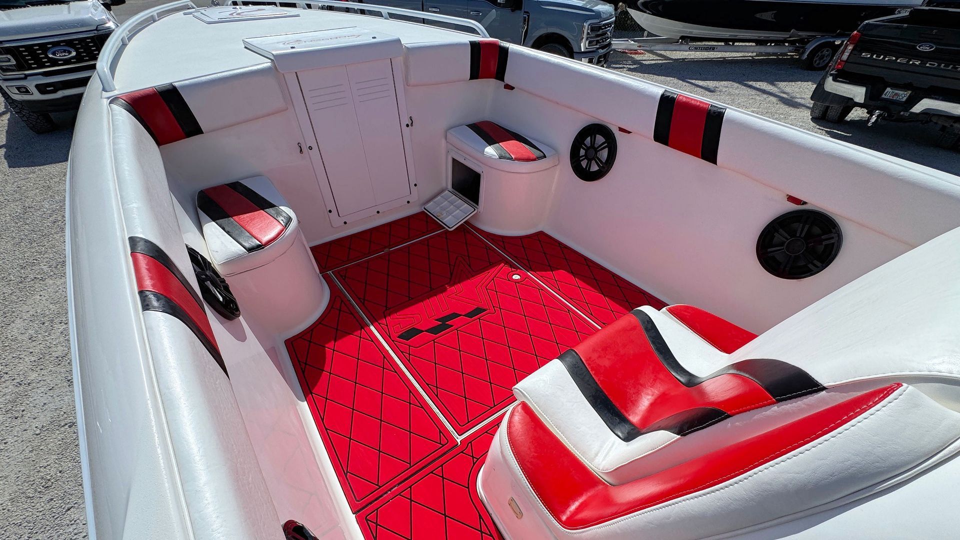 White and red boat cockpit with padded seats, red carpet, and black speakers on the side walls