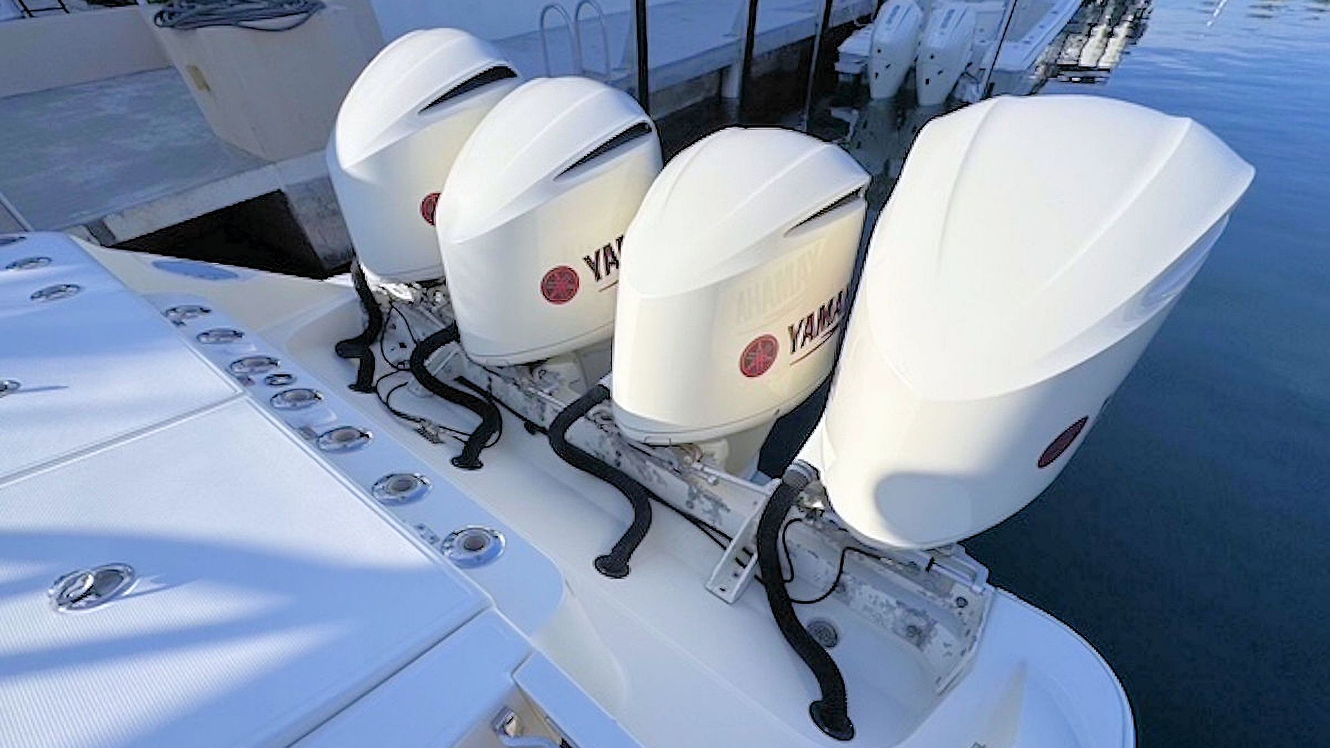 Four white outboard motors mounted on a stern beside calm blue water