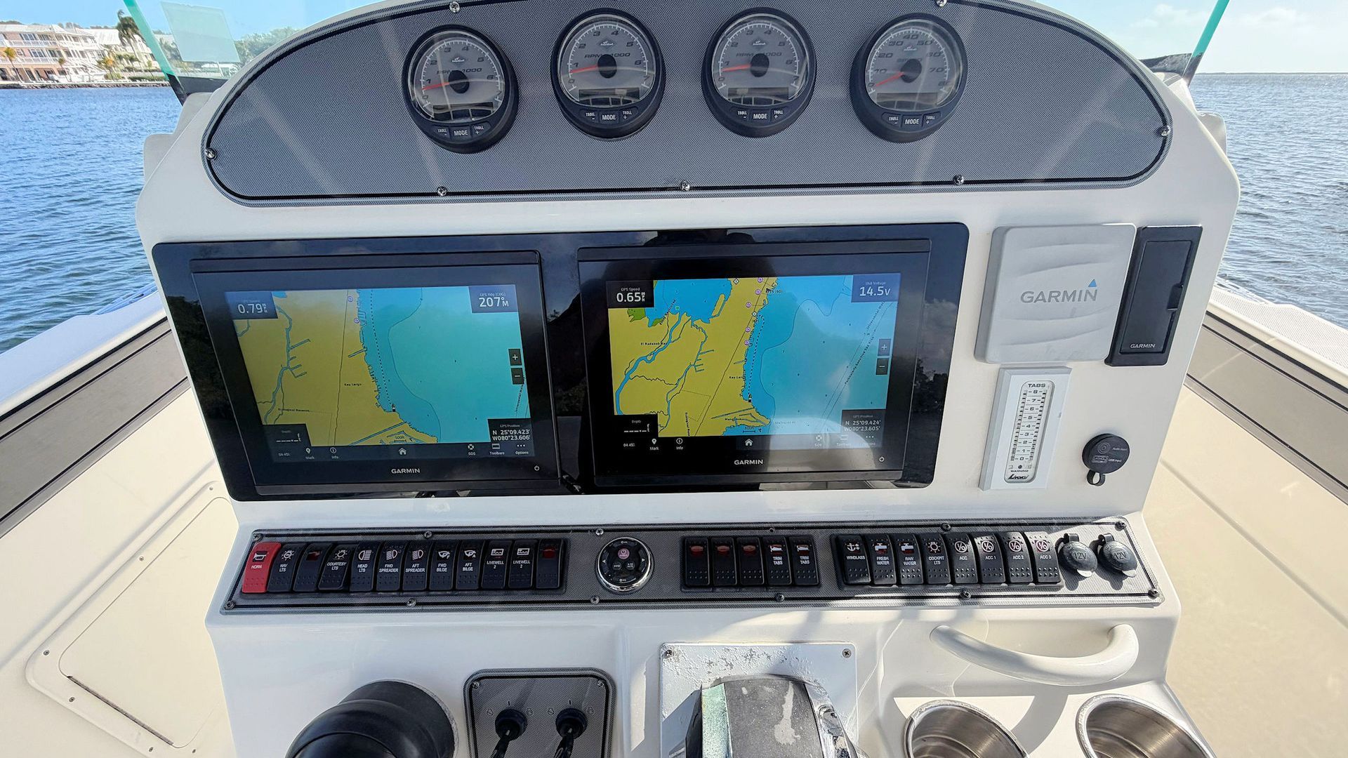 Boat helm with dual navigation displays, gauges, and controls against an ocean background