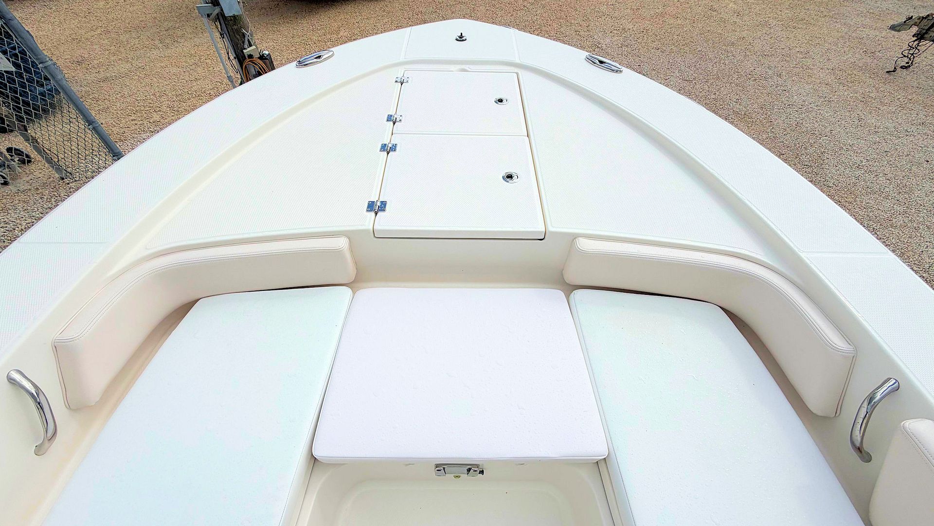 White boat deck with cushioned seating and hatch, viewed from the bow over gravel shore