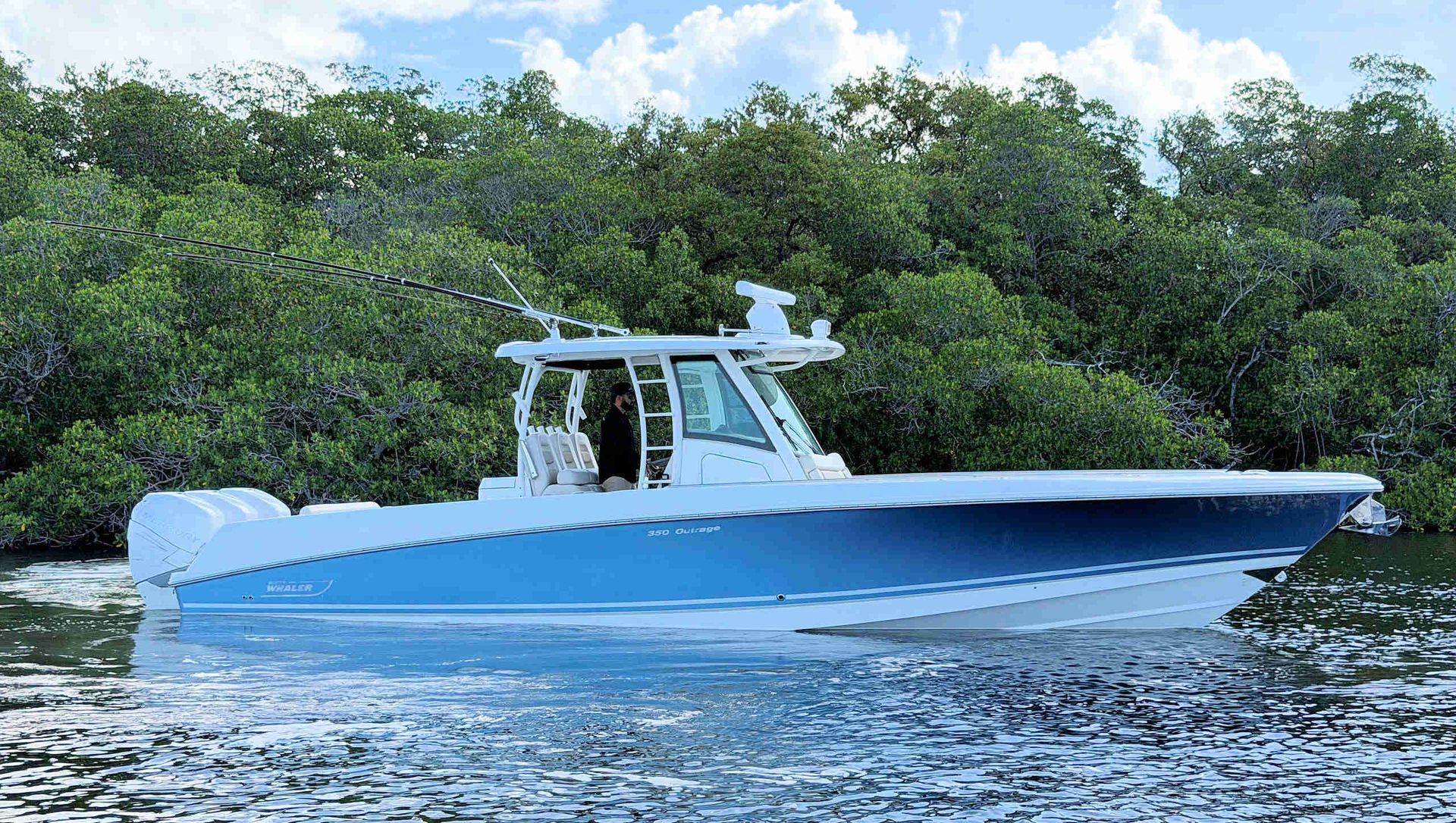 Blue and white fishing boat cruising on calm water near a green shoreline