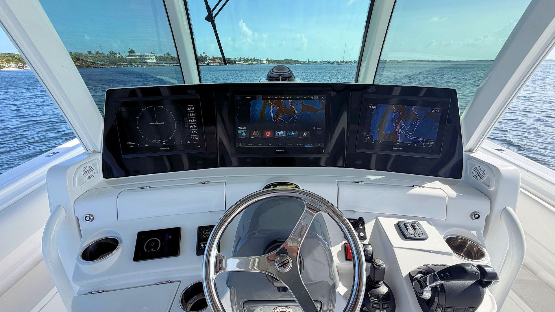 Boat helm with steering wheel and digital displays, facing a bright ocean view through the windshield