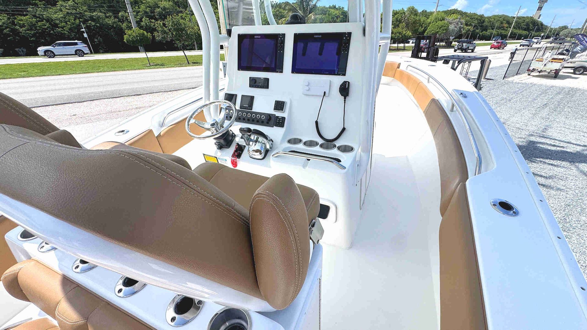Boat helm with white dashboard, dual displays, steering wheel, and tan seating on a sunny day.