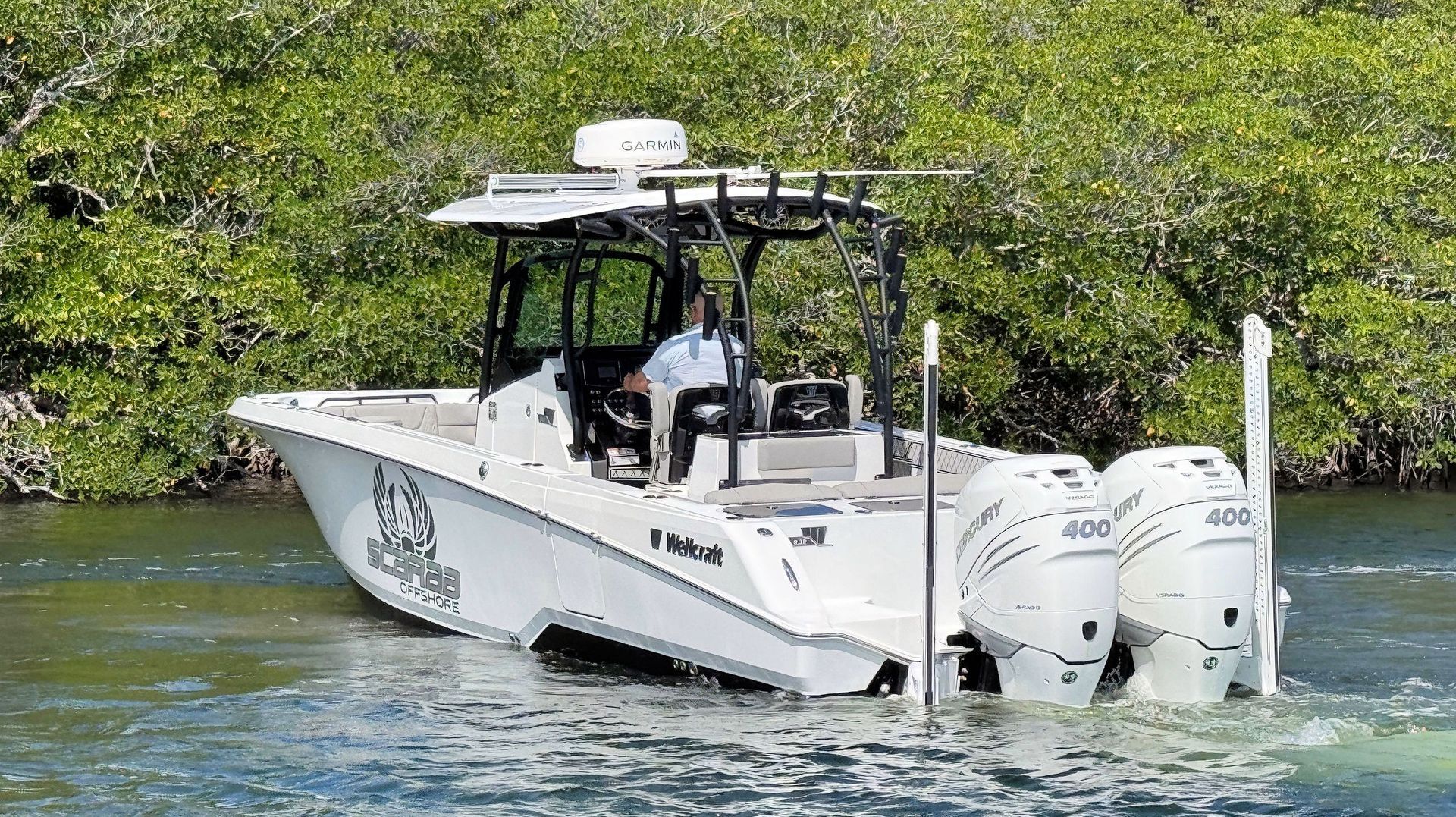 White center-console boat with twin outboard motors on a green river near mangroves