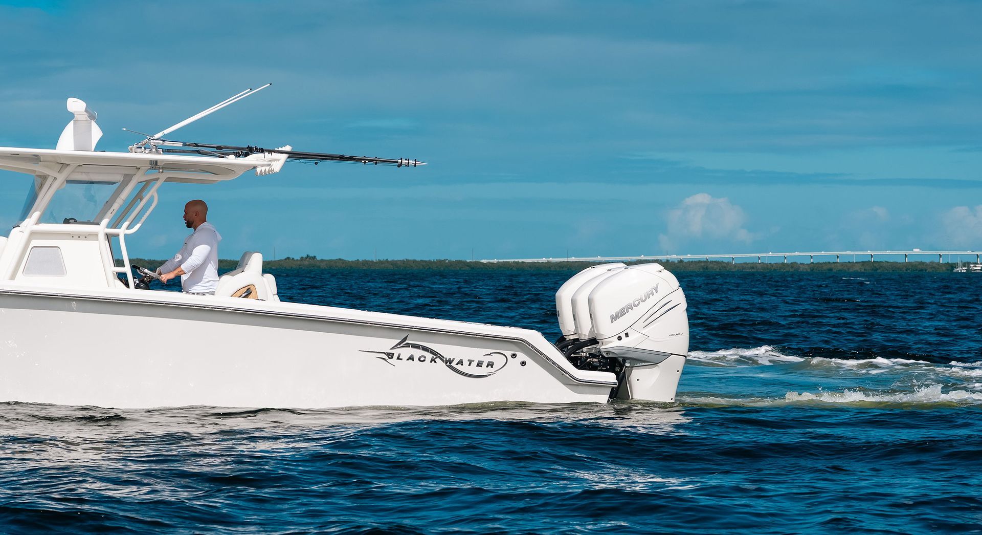 White motorboat with a person aboard speeding across deep blue water under a clear sky