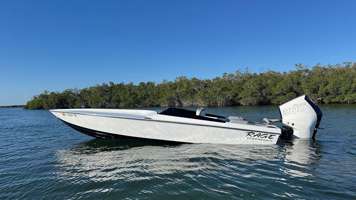 White motorboat on water, blue sky, trees in background.