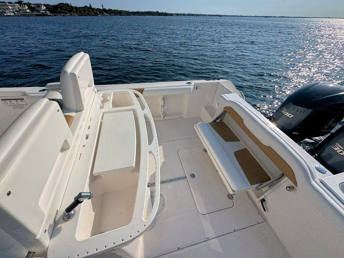Interior view of a white motorboat with open deck, bench seating, and dual  engines on water.