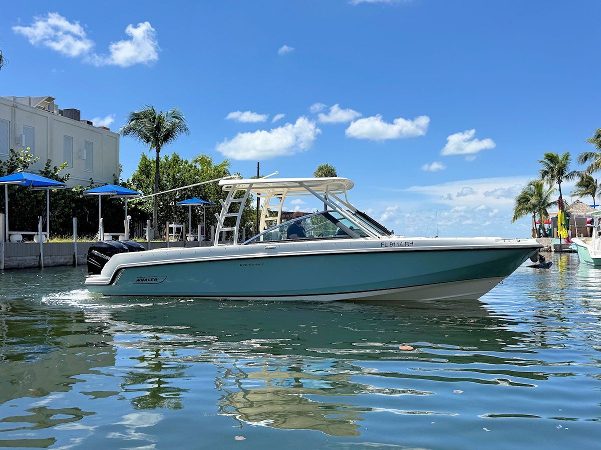 Boat on water, light blue hull, white top, sunny day, clear blue sky, buildings in the background.