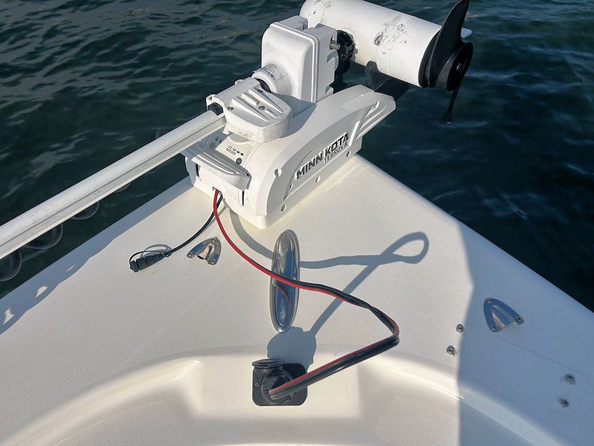 White fishing boat bow with mounted trolling motor and connected cables.