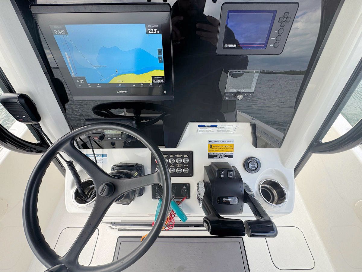 Boat dashboard with steering wheel, navigation screens, and control panel.