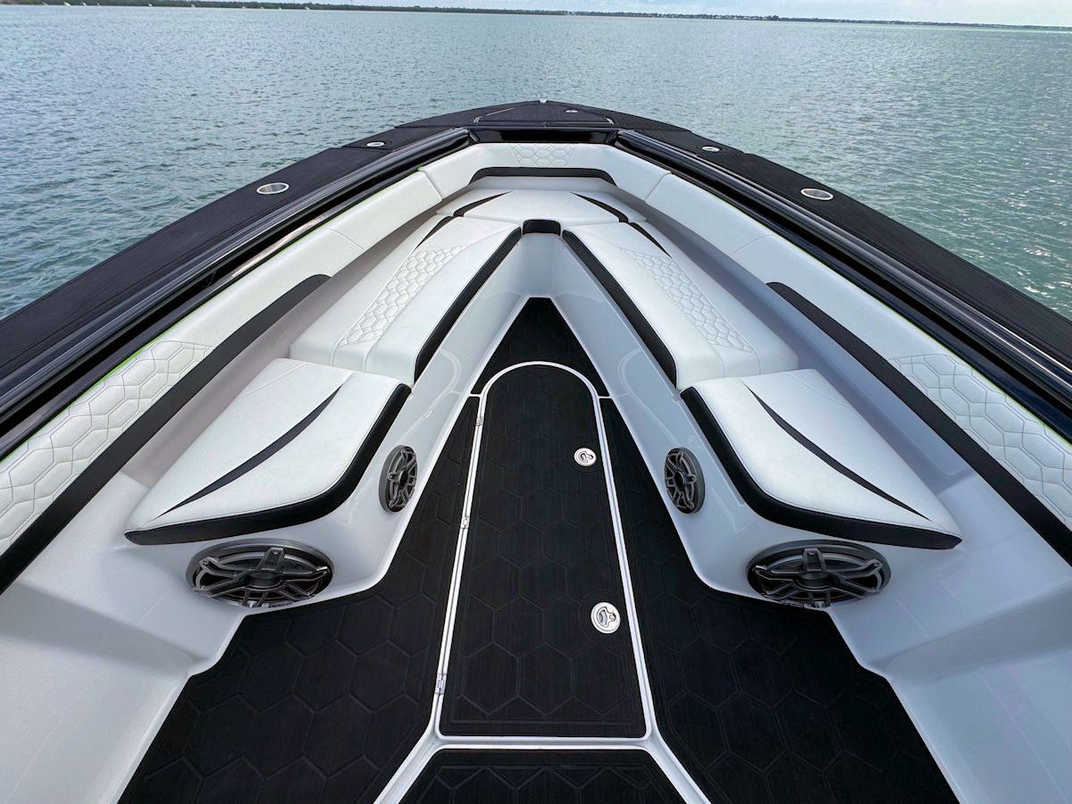 Bow seating of a boat with white and black upholstered seats, black flooring, and speakers.