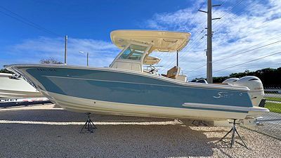 A light blue and white motorboat parked on a gravel lot under a bright, blue sky.
