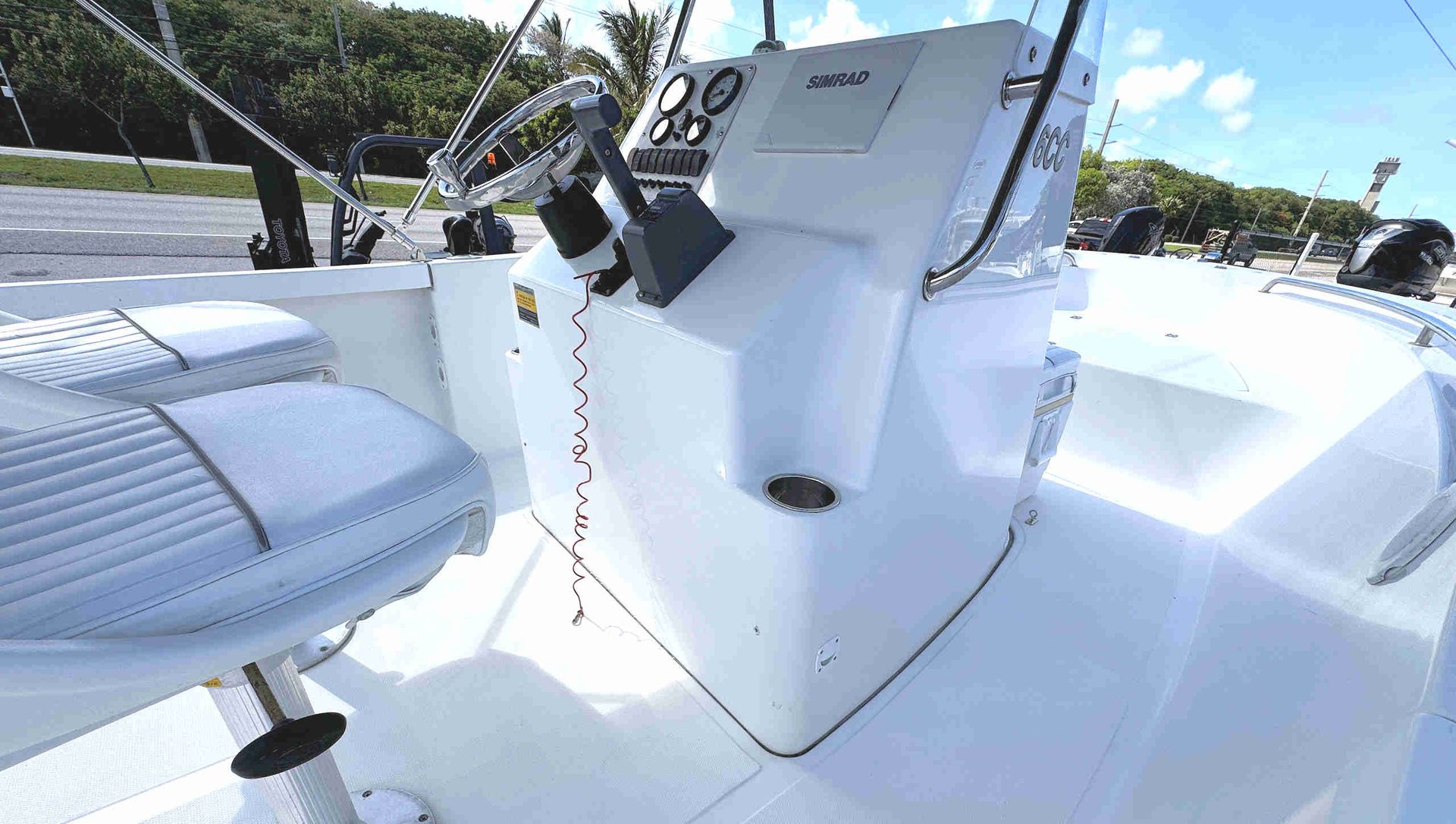White Tidewater skiff center-console with steering wheel, controls, and a cushioned seat under bright sunlight