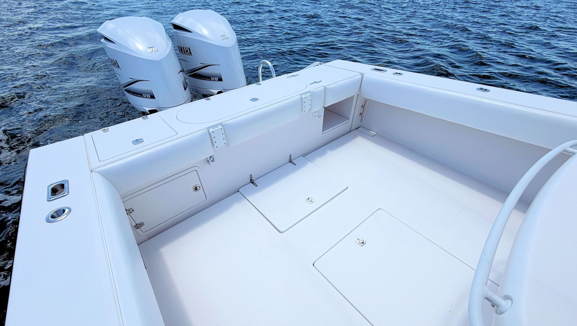Aftdeck of a fishing boat stern with with livewells and twin outboard motors on blue water