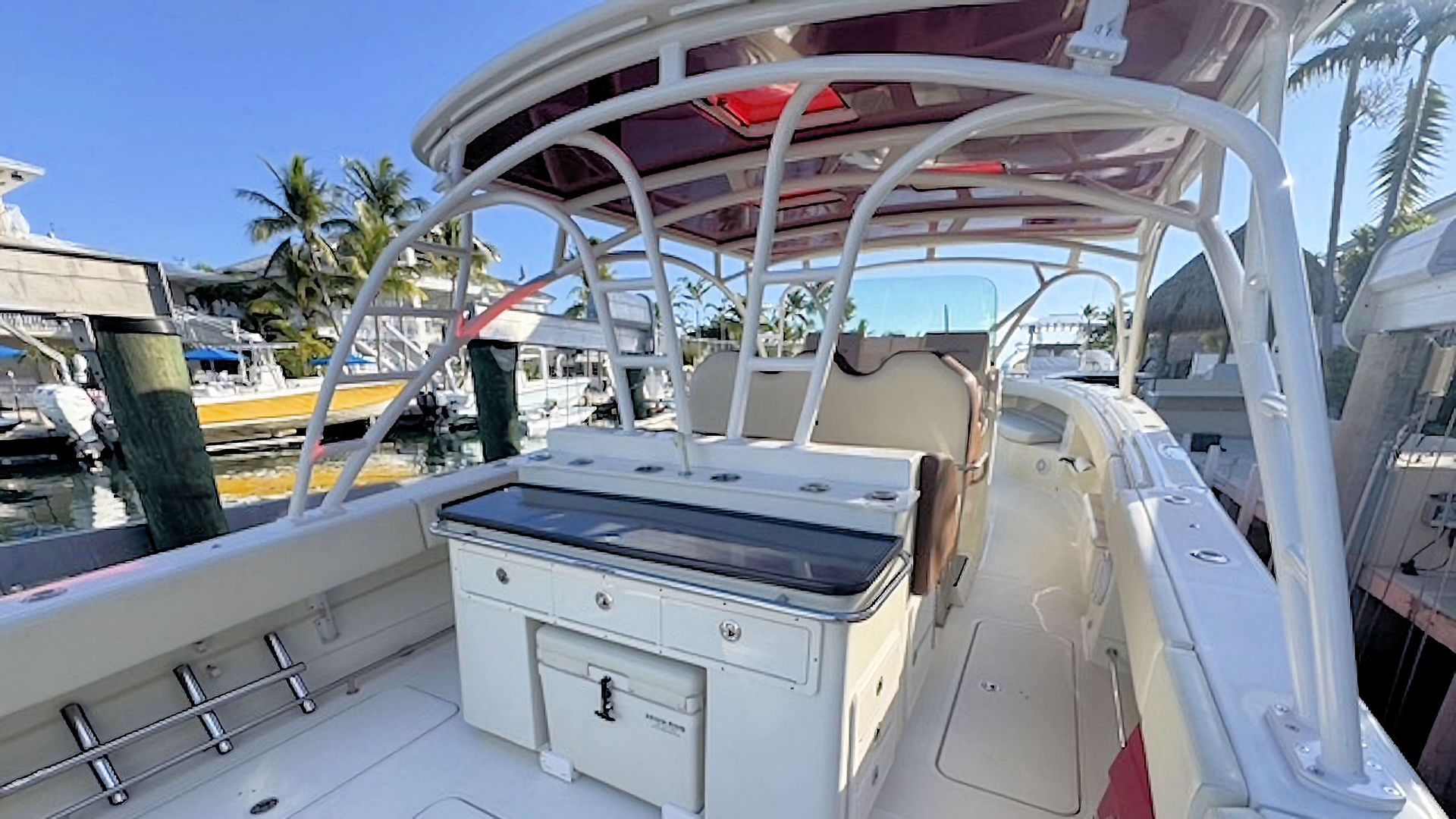White boat deck with cushioned seating, storage console, and overhead canopy near a marina