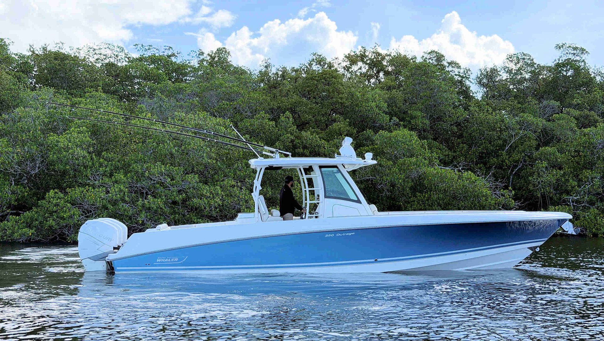 Blue and white fishing boat cruising on calm water near a green shoreline