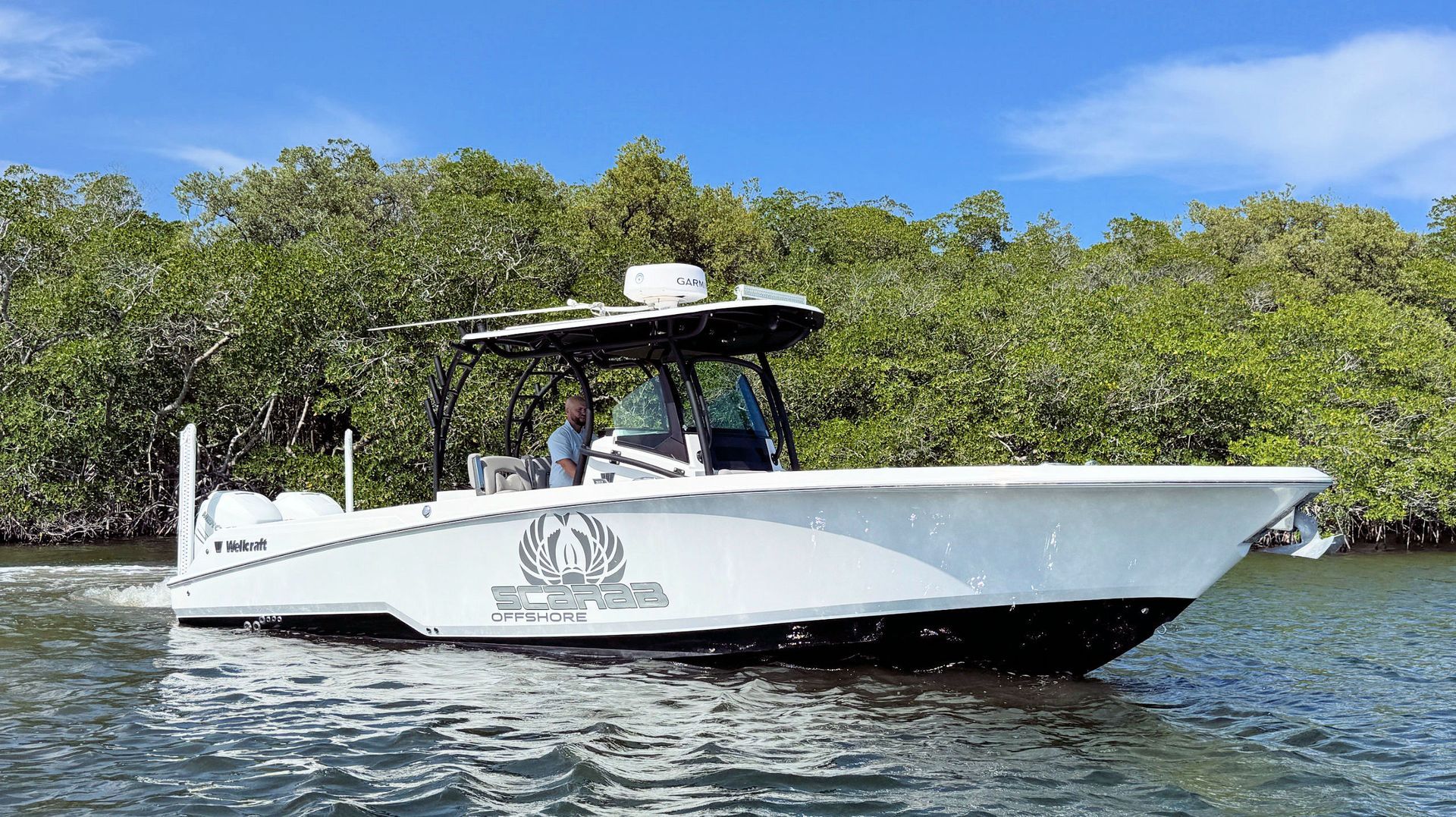 White fishing boat cruising on water near a mangrove-lined shore under a blue sky