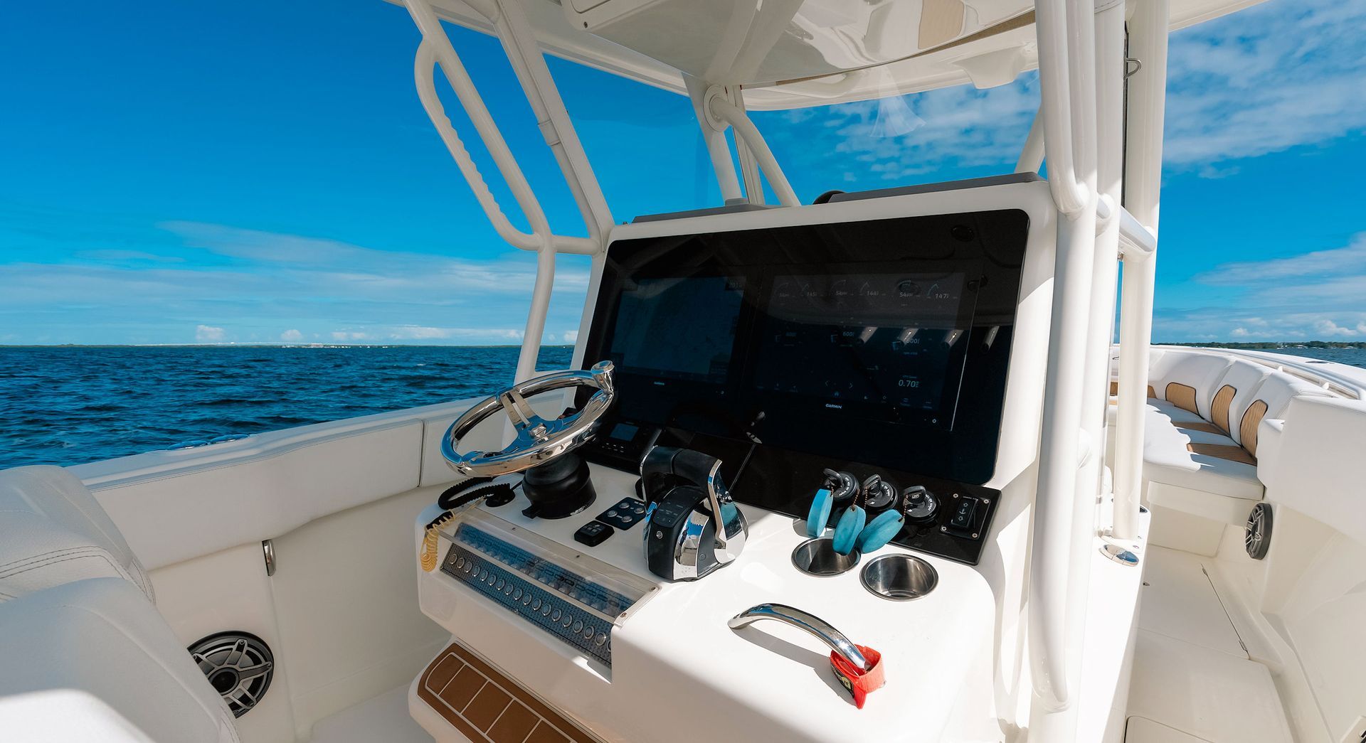 Boat helm with steering wheel and controls on a white yacht, ocean visible ahead under a blue sky