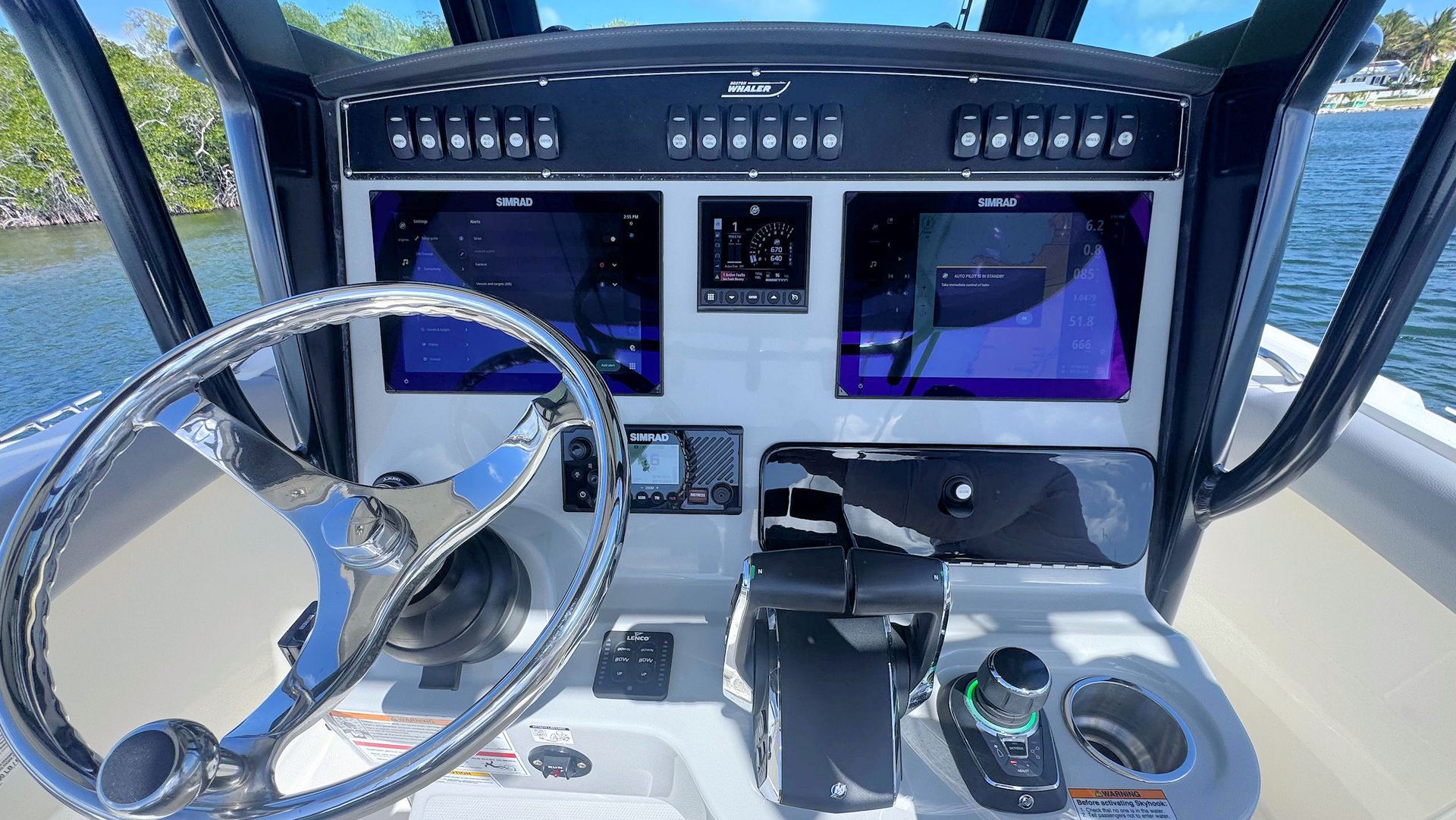 A boat helm featuring a chrome steering wheel, two large navigation screens, switch controls, and a throttle console.