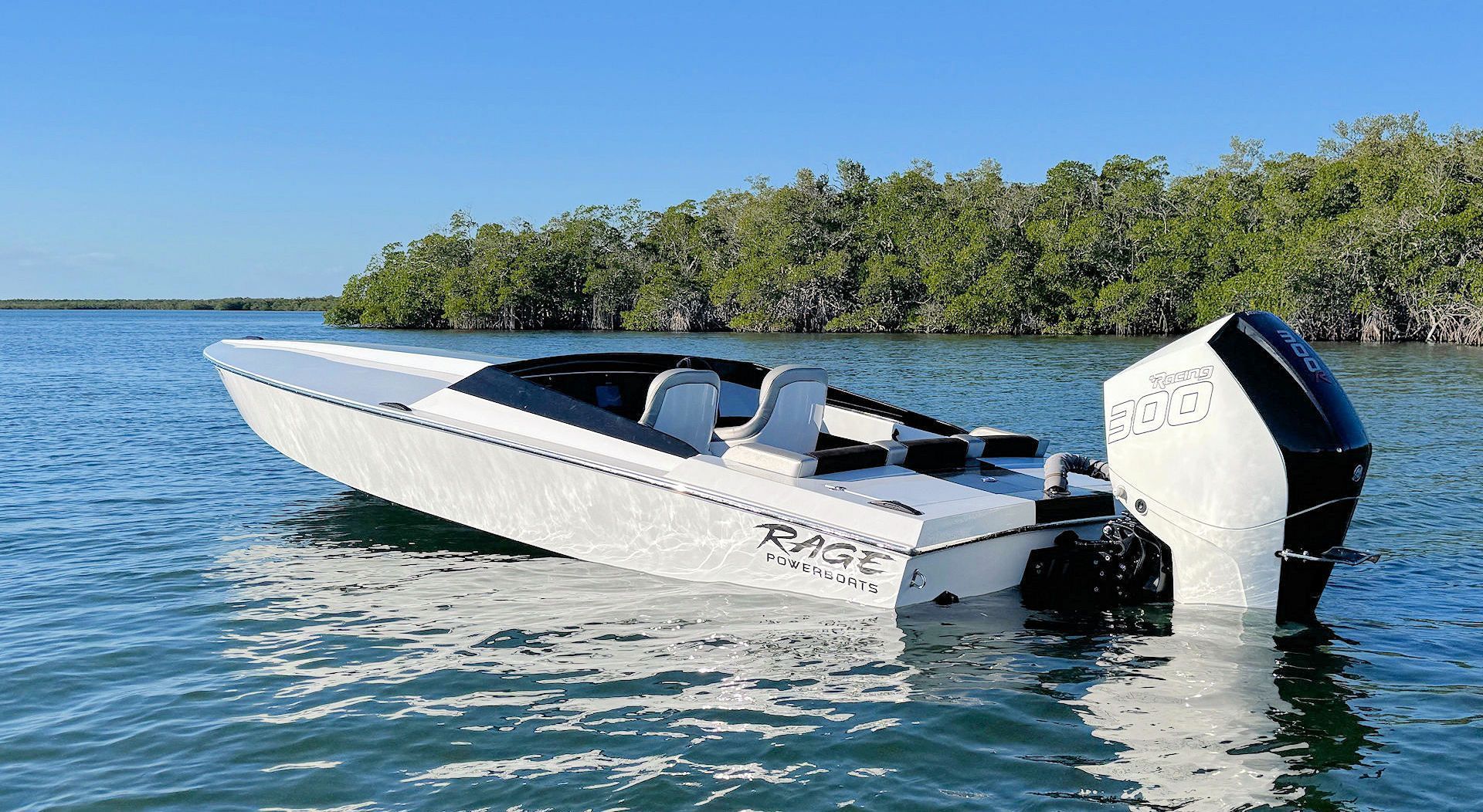 A white and black performance powerboat with a large outboard motor floating in calm, blue water near a mangrove forest.