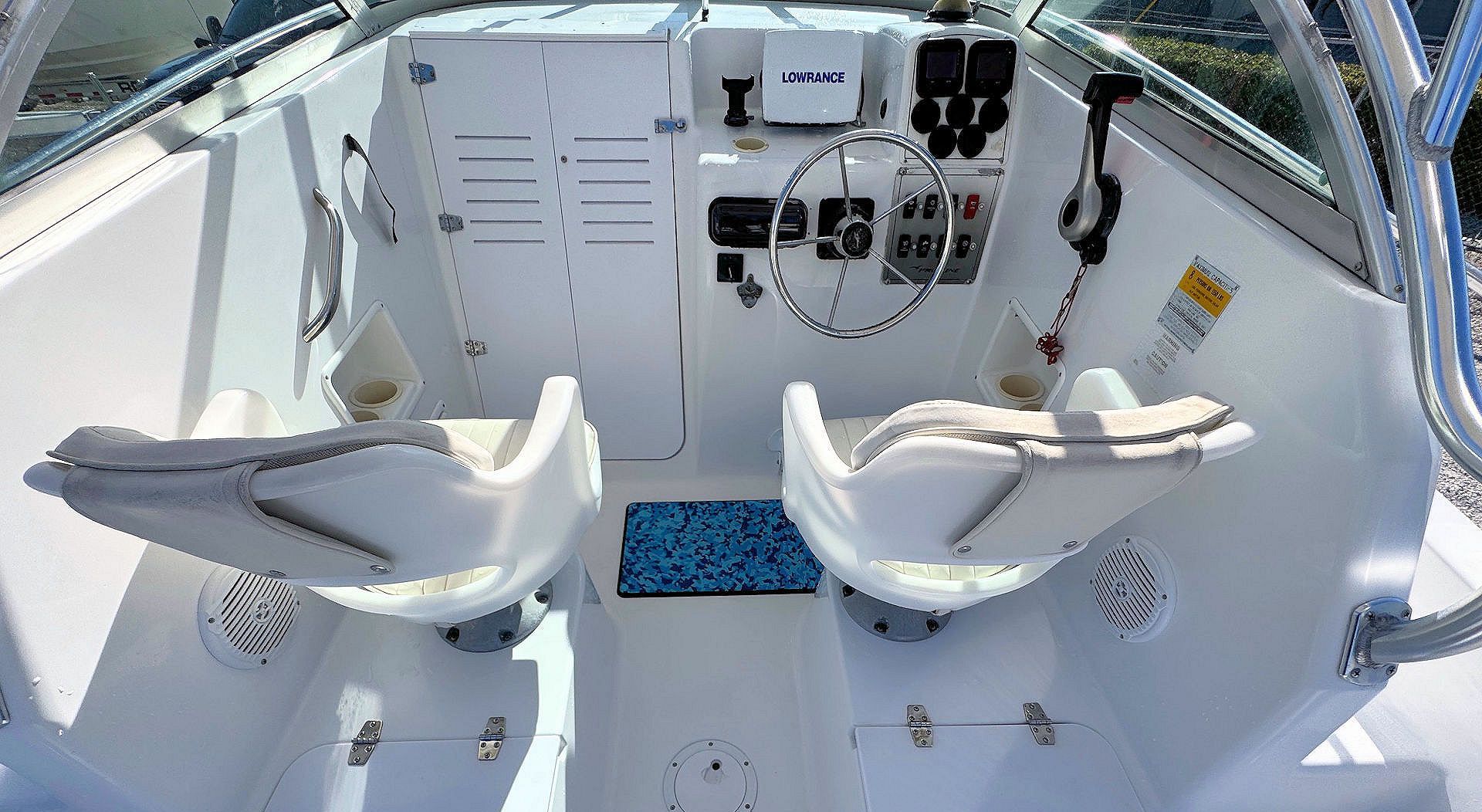The help of a white boat, featuring two captain's chairs, a steering wheel, a digital display, and controls.