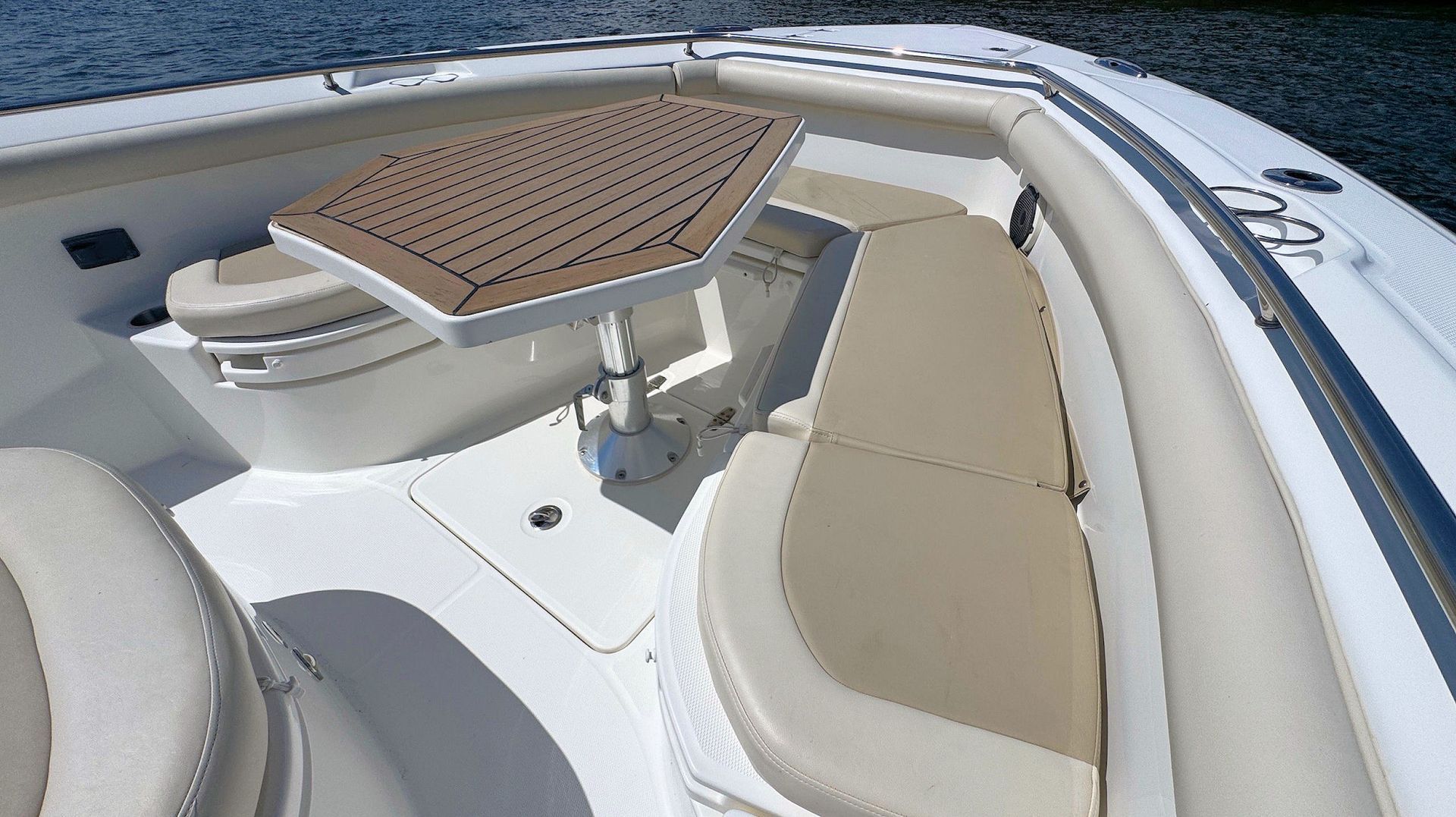 Bow with beige cushioned seating, white deck, and a wooden table under bright sunlight