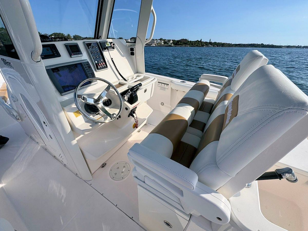Boat interior with steering wheel, gauges, and white and tan seating; sunny day on the water.