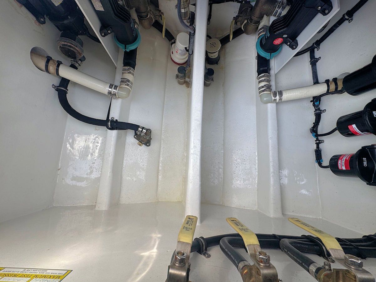 Interior view of a boat's machinery compartment with pipes, valves, and components. White surfaces and dark tubing.