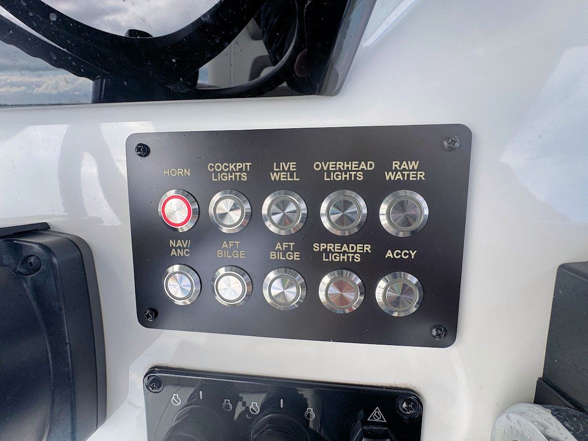 Black control panel on boat dashboard with labeled switches, including lights and pumps.
