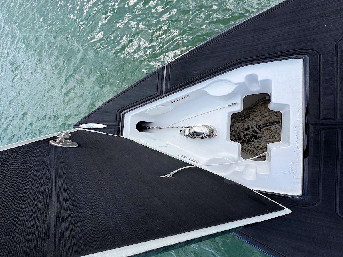 Boat anchor in a white compartment, with black deck, on the water.