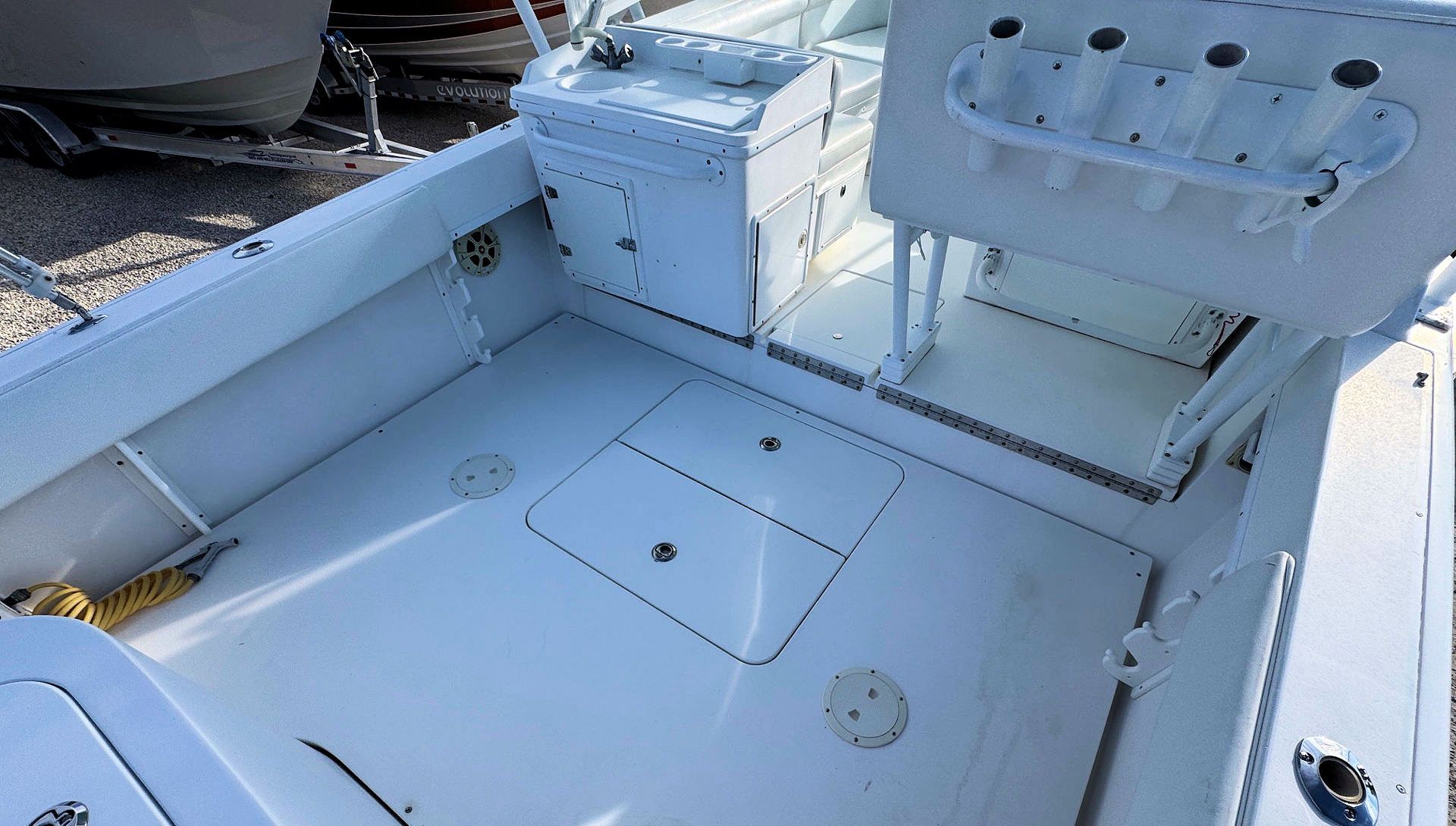 White boat deck with storage hatches, rod holders, and a mounted seat in bright sunlight