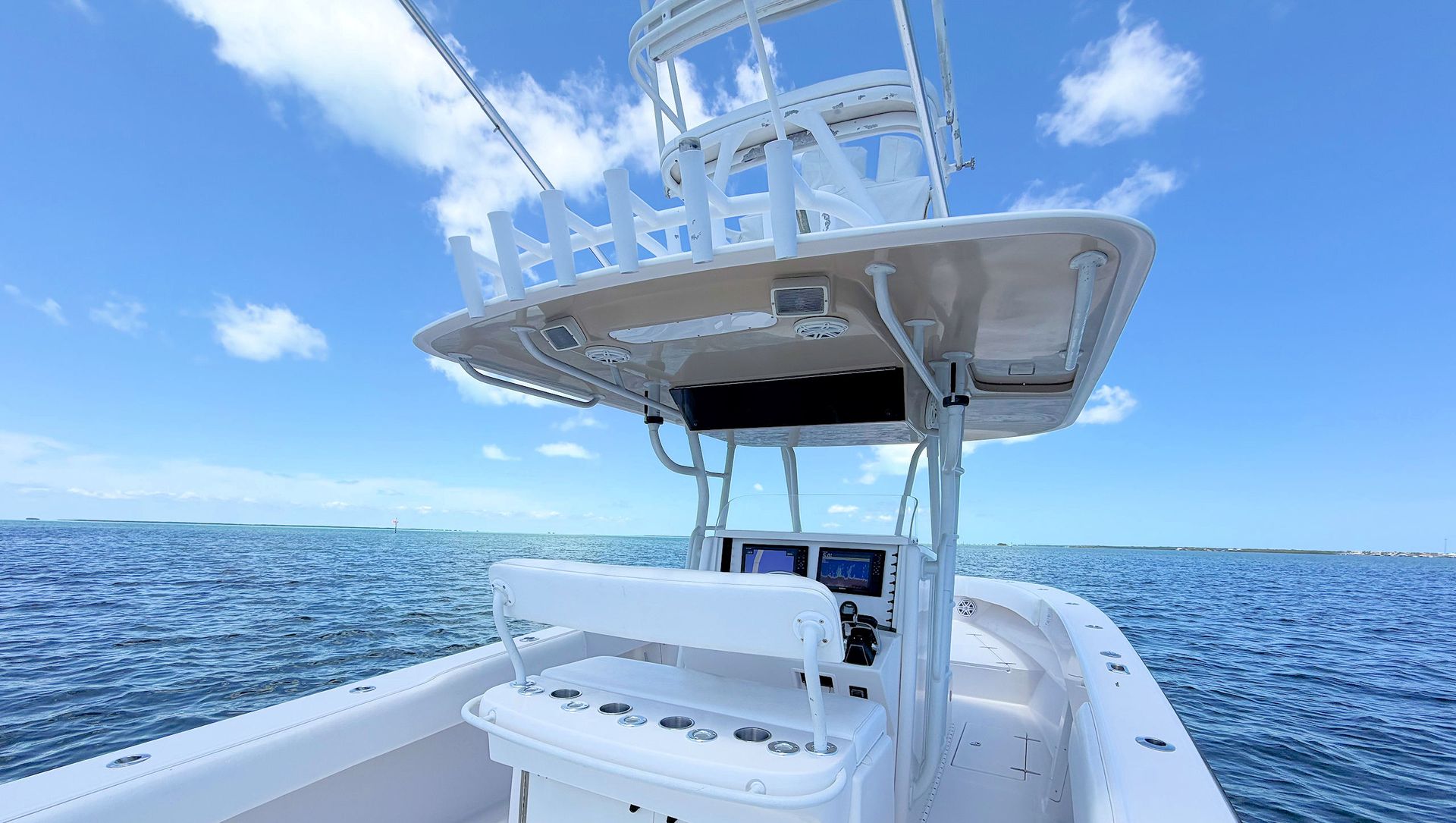 View from the aftdeck towards the helm, t-top and upper station controls over open ocean under a bright blue sky