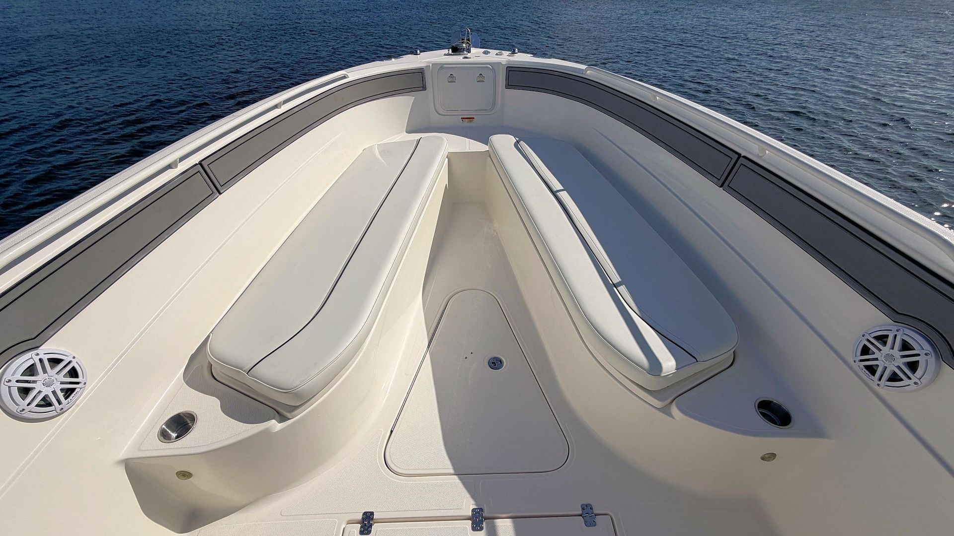 Front deck of a white boat on open water, with cushioned lounge seats and speakers.