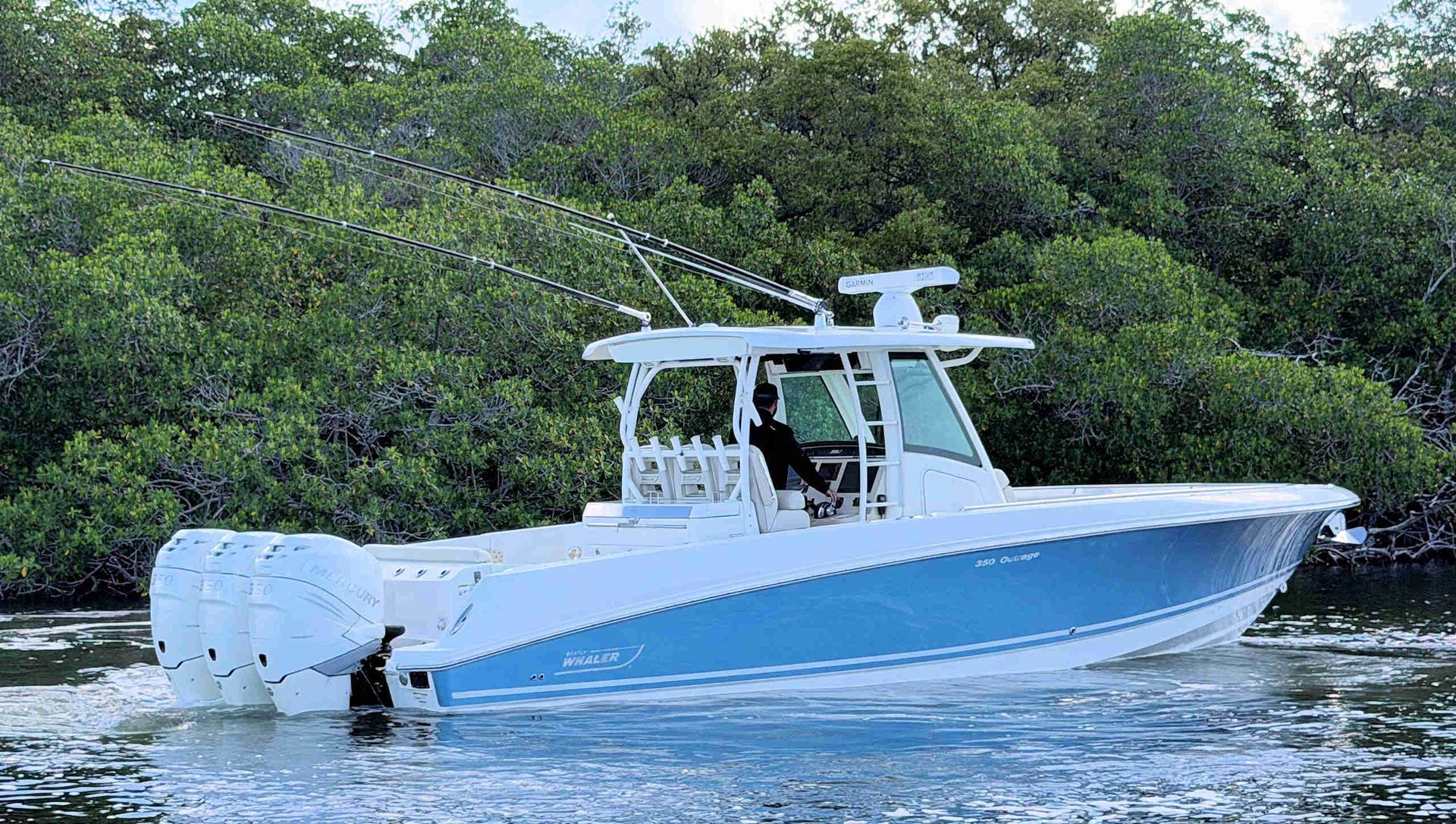 White-and-blue center console boat cruising on calm water near mangrove-lined shore