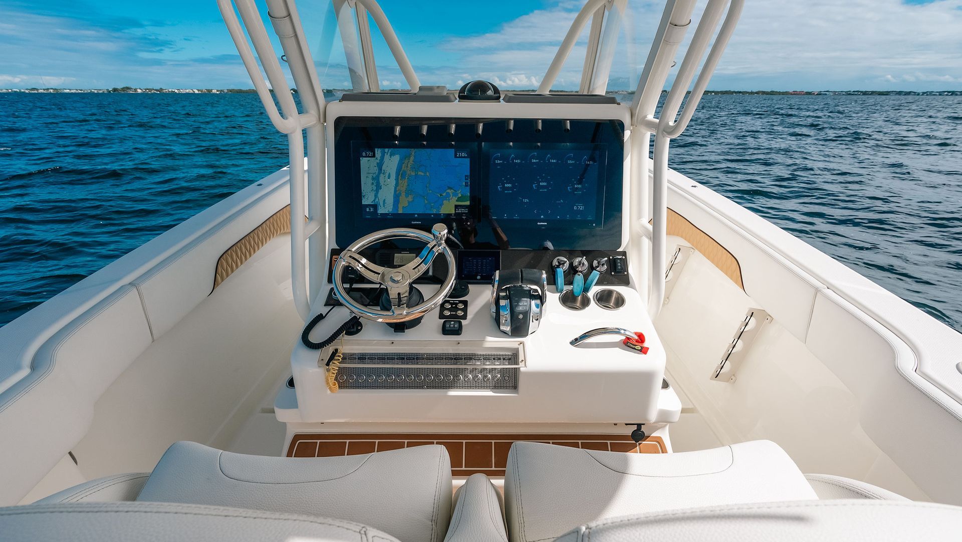 Boat helm with steering wheel and navigation screen on a white yacht, ocean visible ahead.
