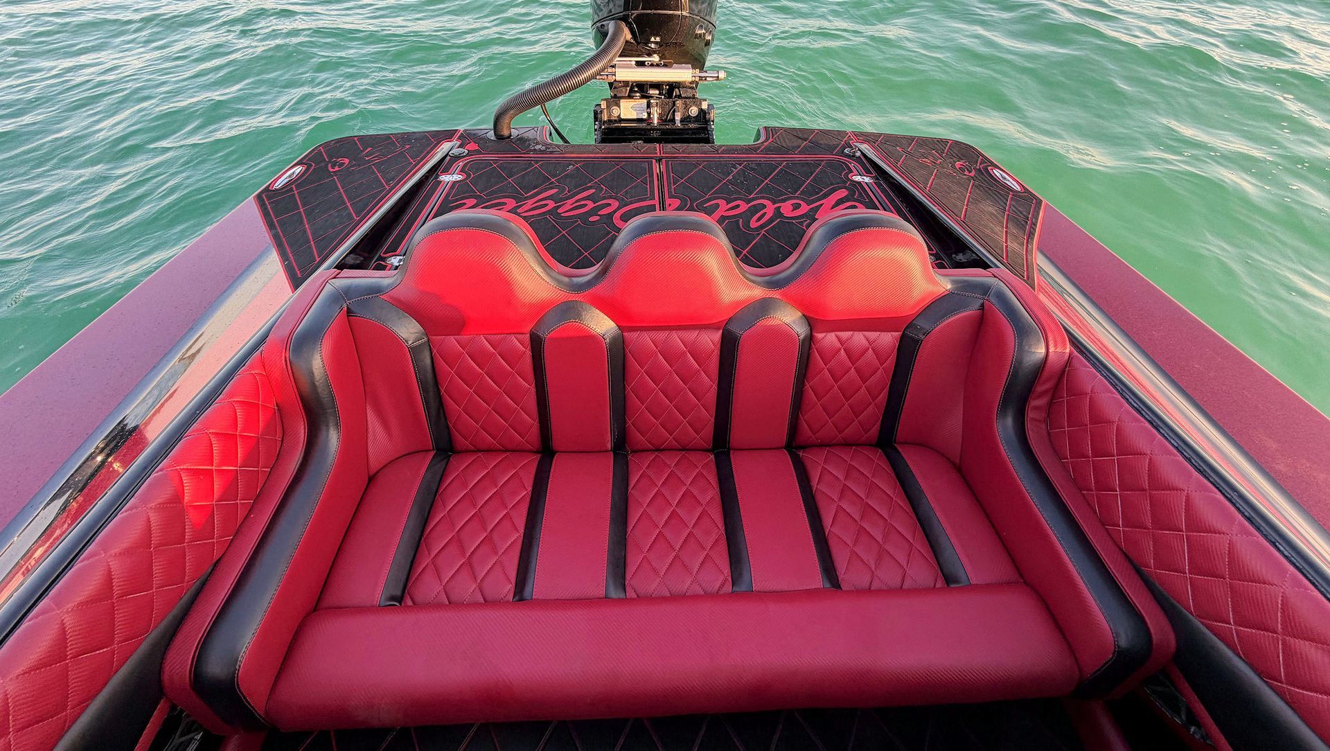 Red cushioned boat seating facing turquoise water, with black trim and a rear view of the deck.