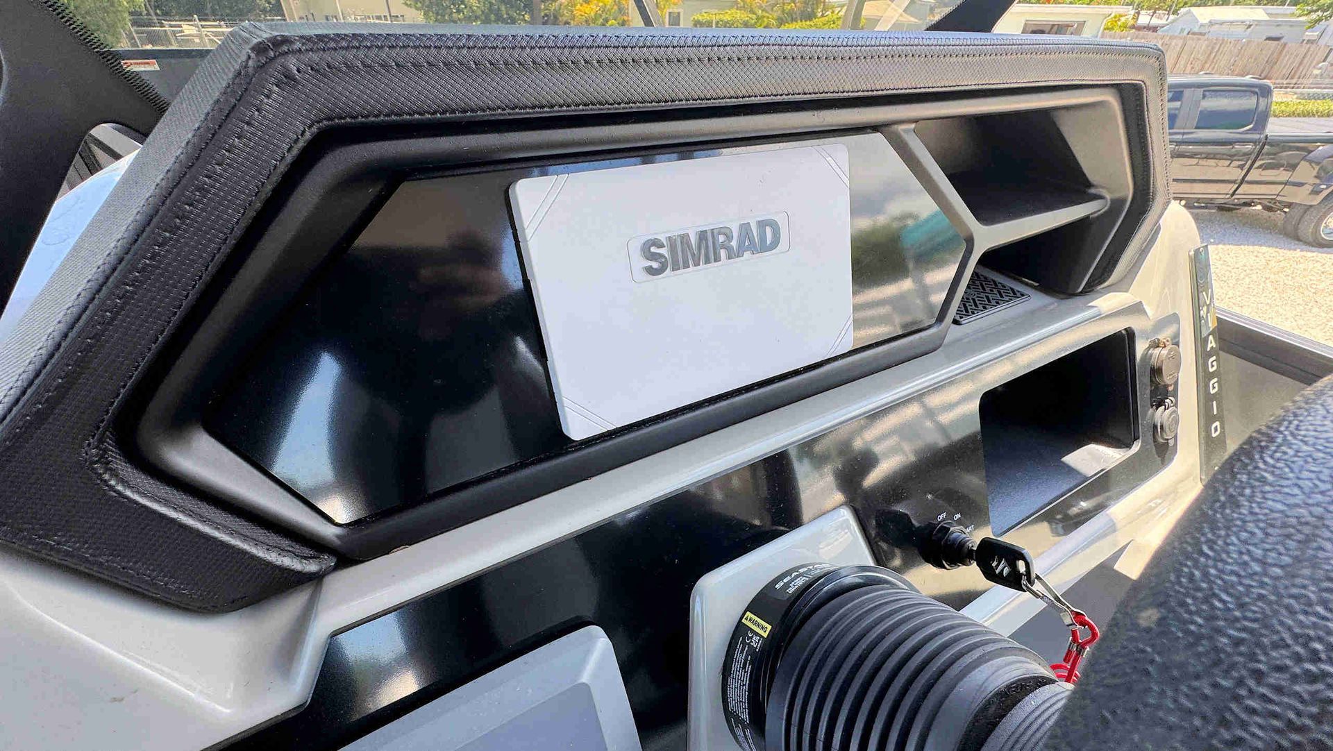 Close-up of a boat helm with a SIMRAD display and steering wheel in sunlight