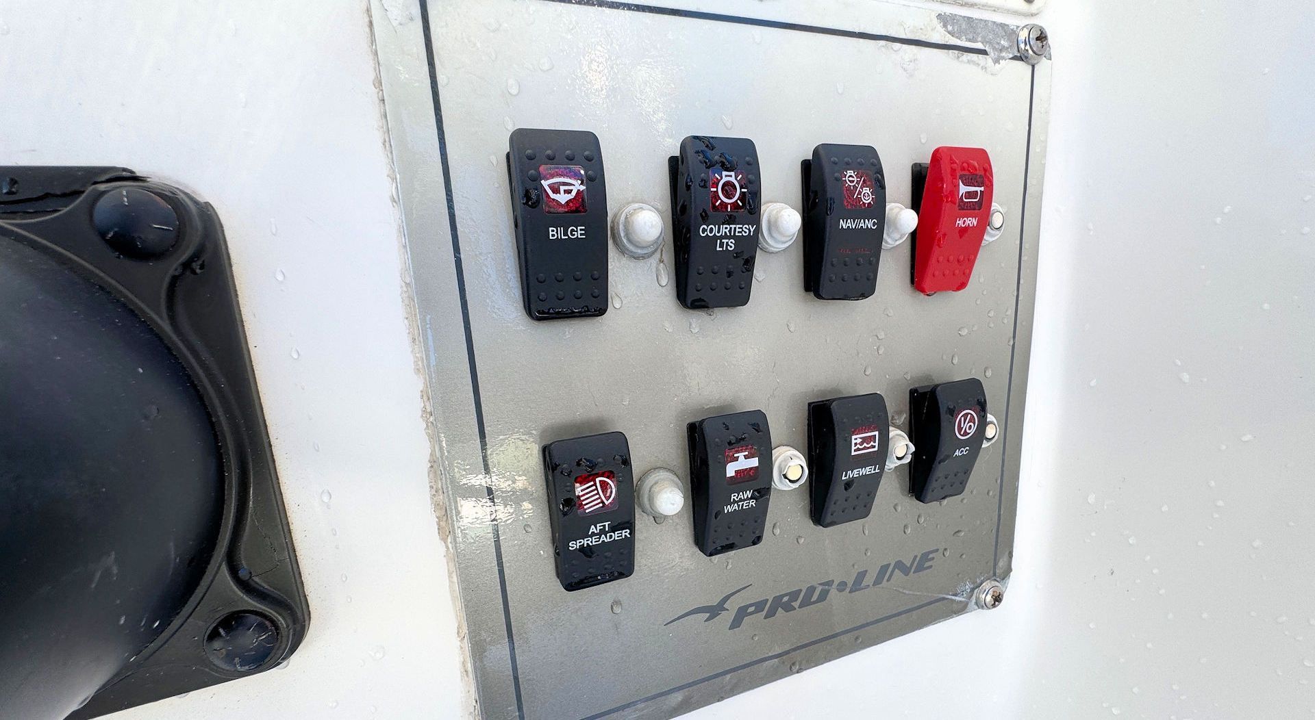 A silver boat dashboard panel with eight rocker switches, one of which is red, featuring small white equipment icons.