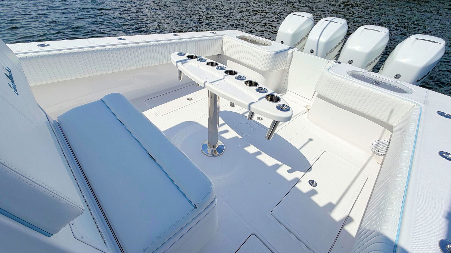 Boat cockpit with white seats, blue cushion, and fishing rod holders under bright sunlight