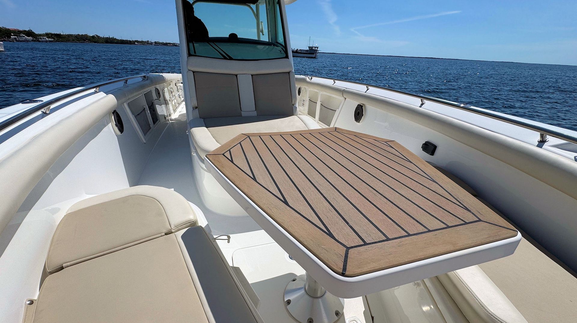 Boat deck with cushioned bench and wooden table on open water under a clear blue sky