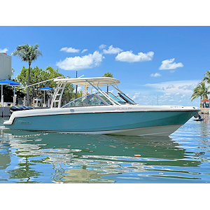White speedboat on calm water with blue sky and light foliage in the background.