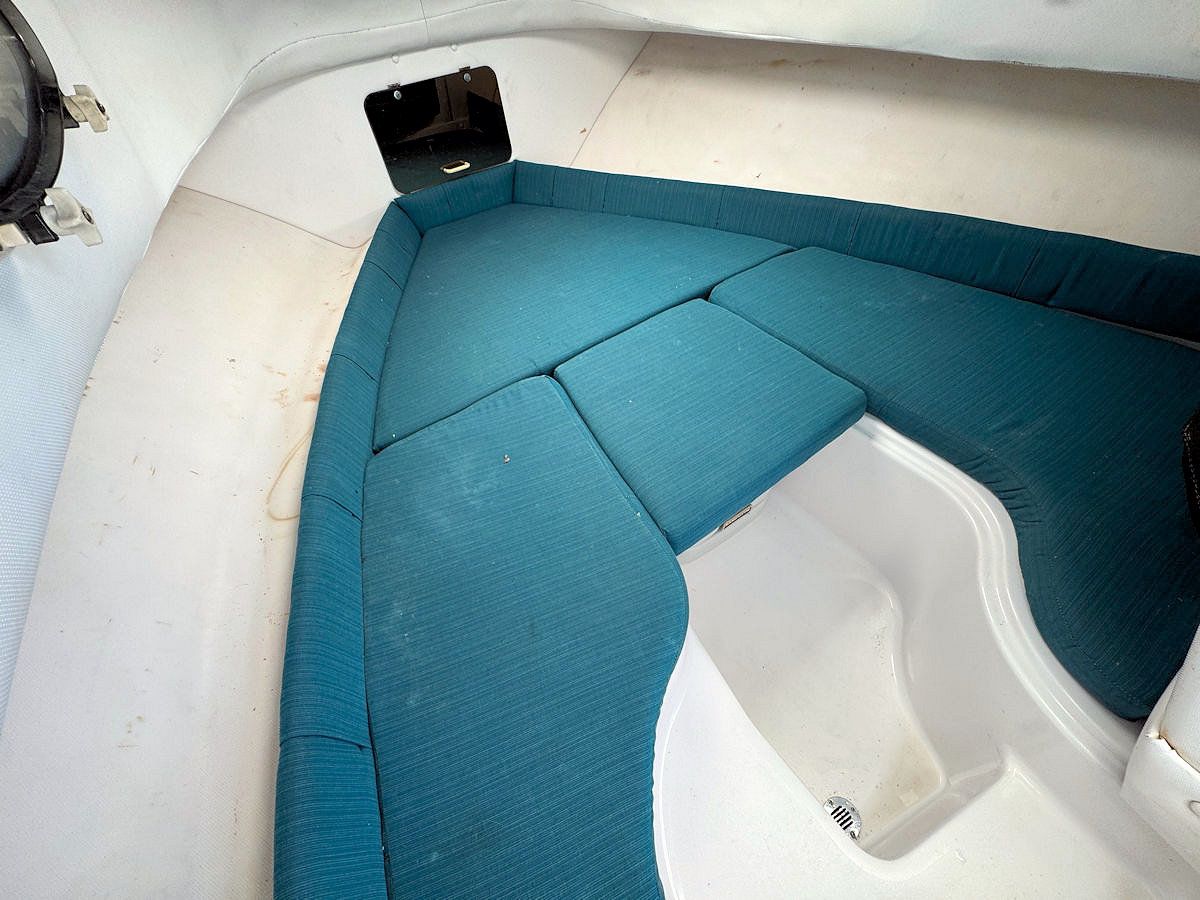 Interior of a boat with teal cushions and white walls. A small open compartment is visible.