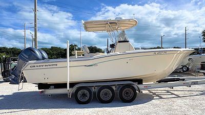 Cream-colored Grady-White boat on a trailer, with twin blue outboard motors, under a light blue sky.