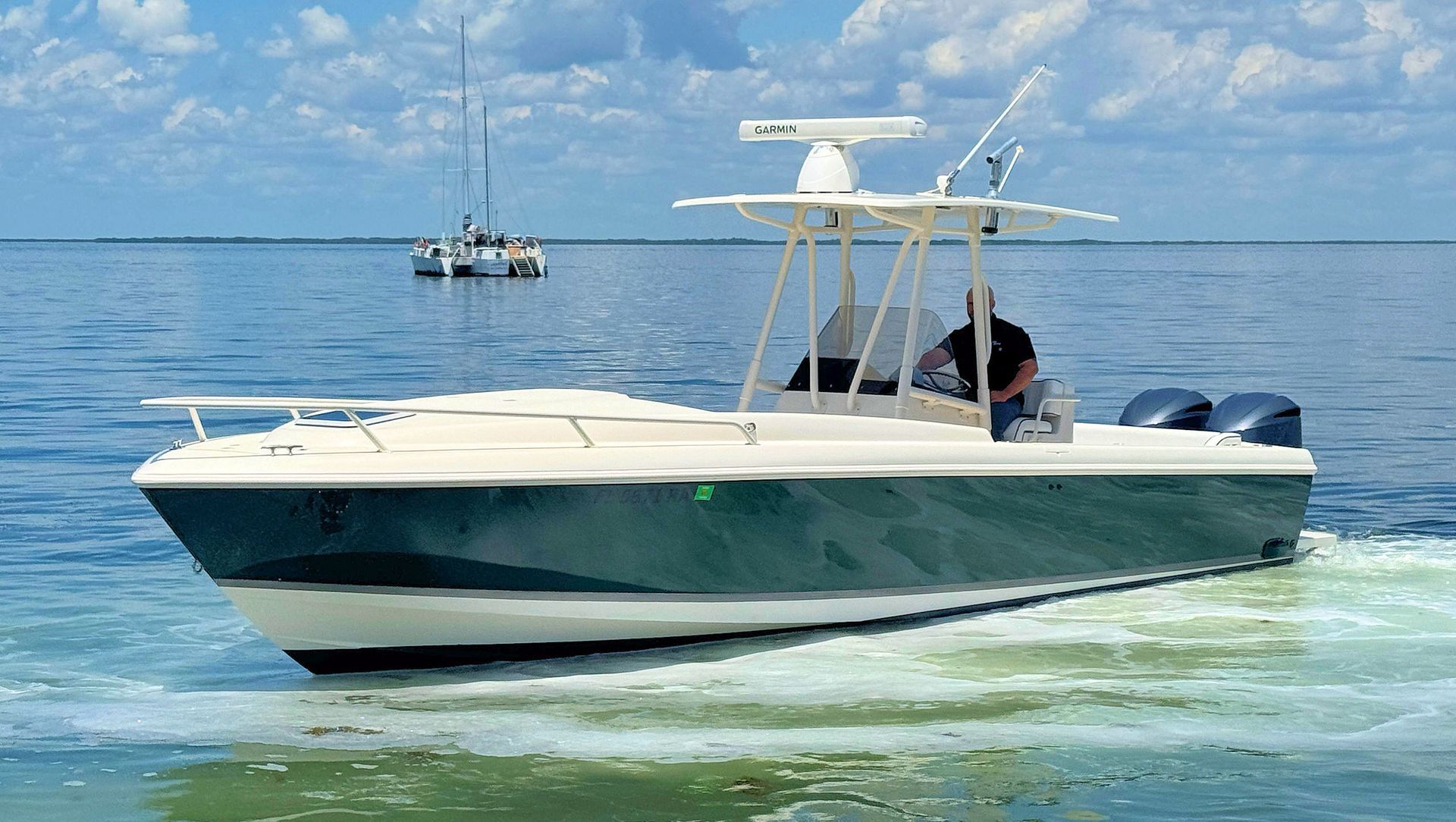 White and navy center console boat cruising on calm blue water under a clear sky, with another boat in the distance