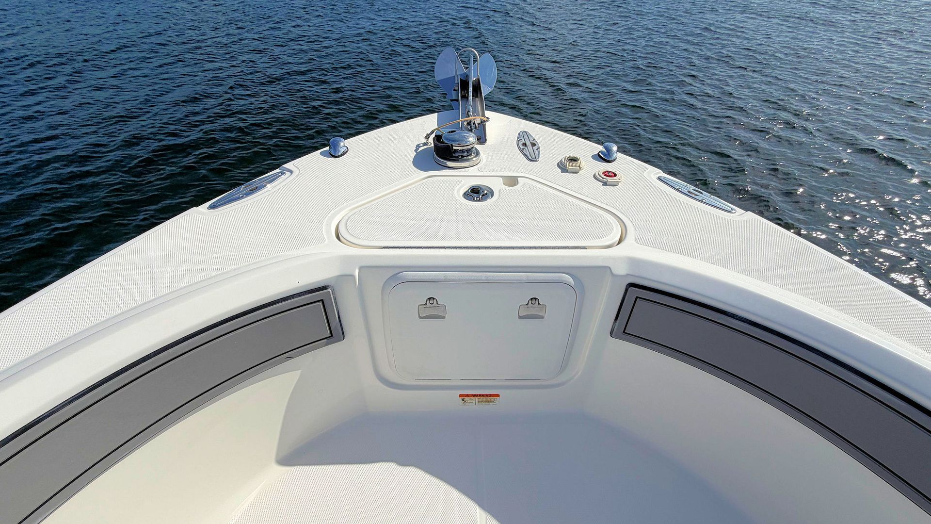 Boat bow deck with white railings and a hatch, facing open water.