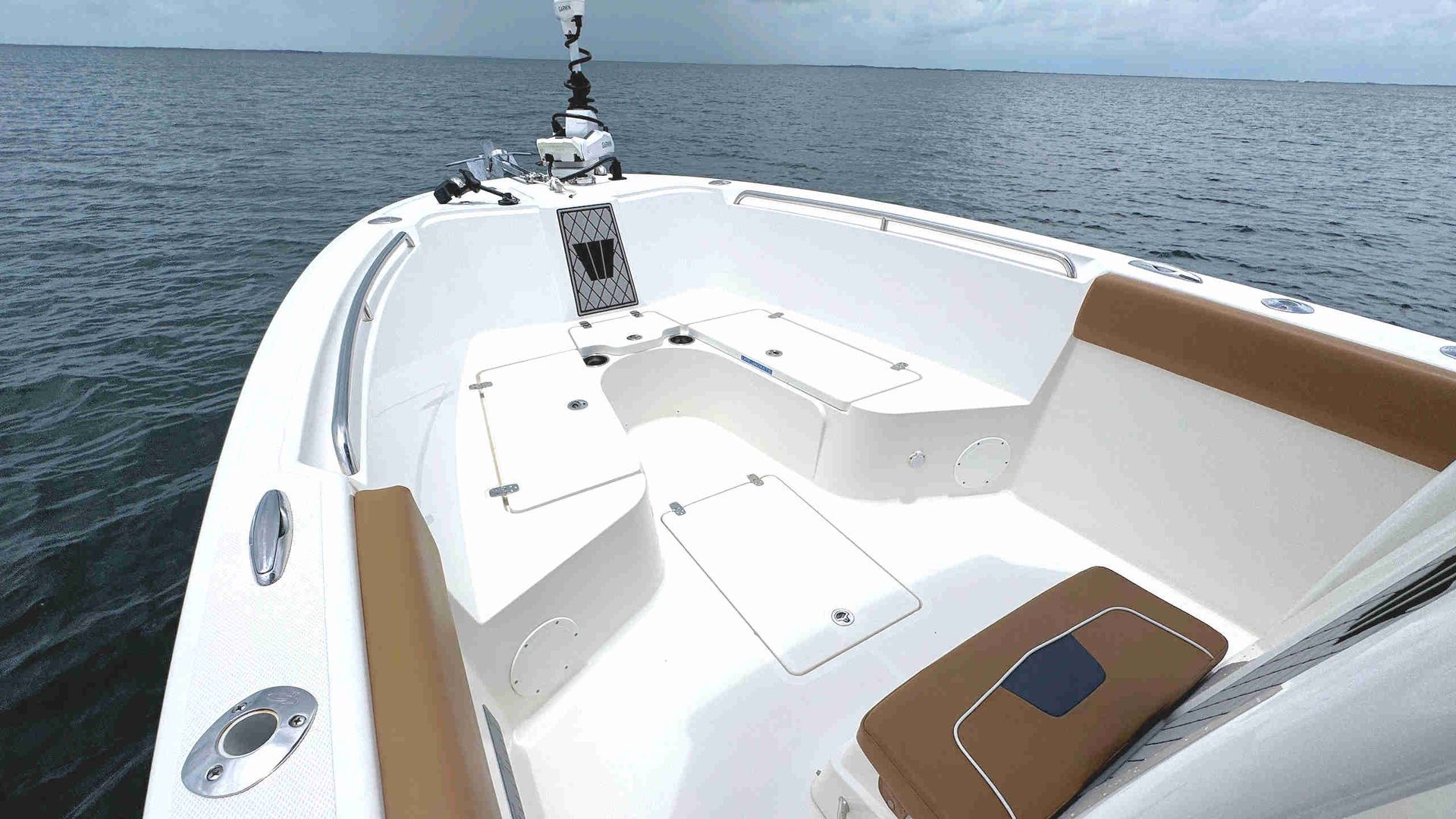 White boat deck with cushioned seating and a tan accent panel on calm water under a clear sky