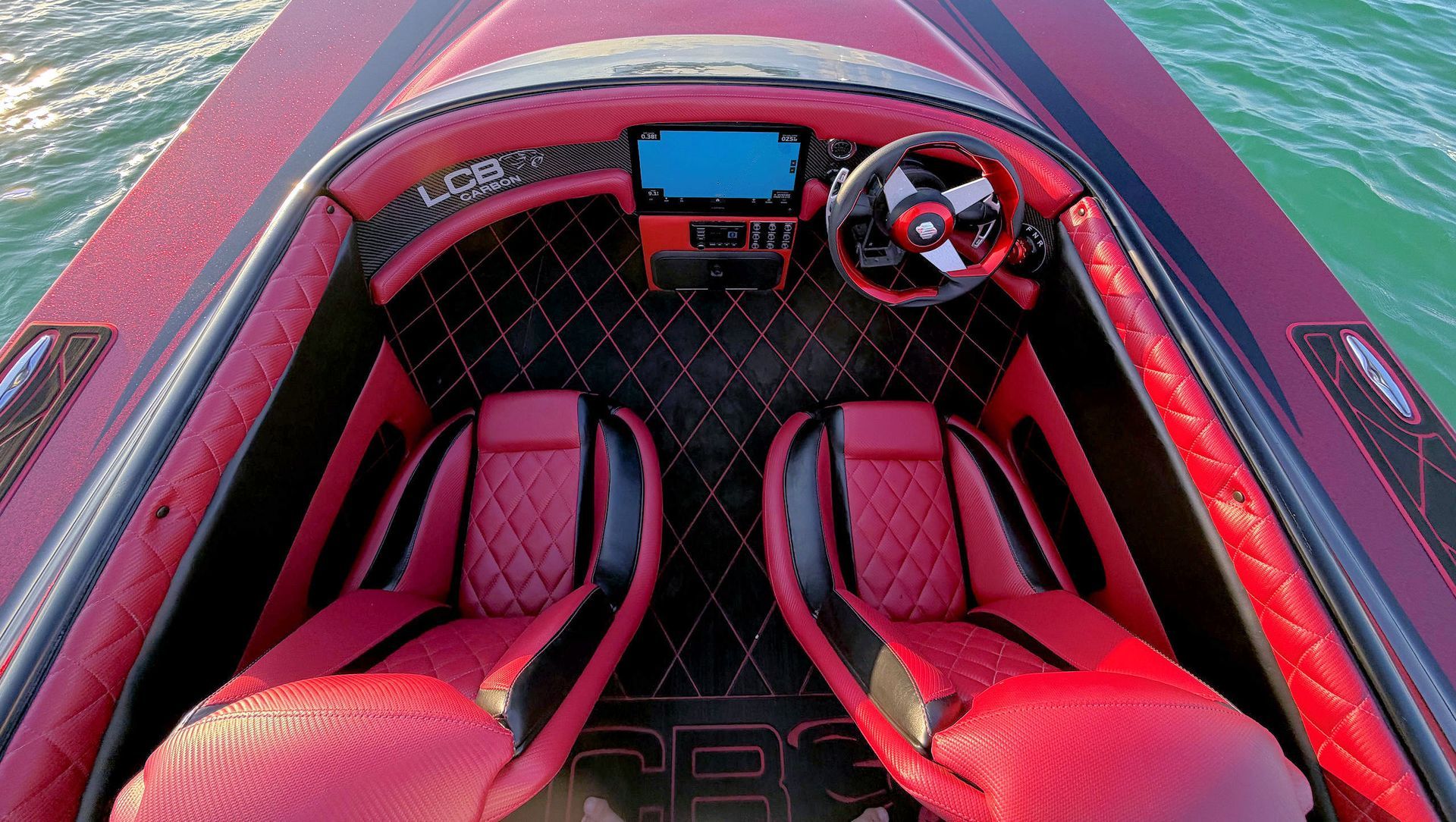 Red and black boat interior with two seats, steering wheel, and dashboard view from above.