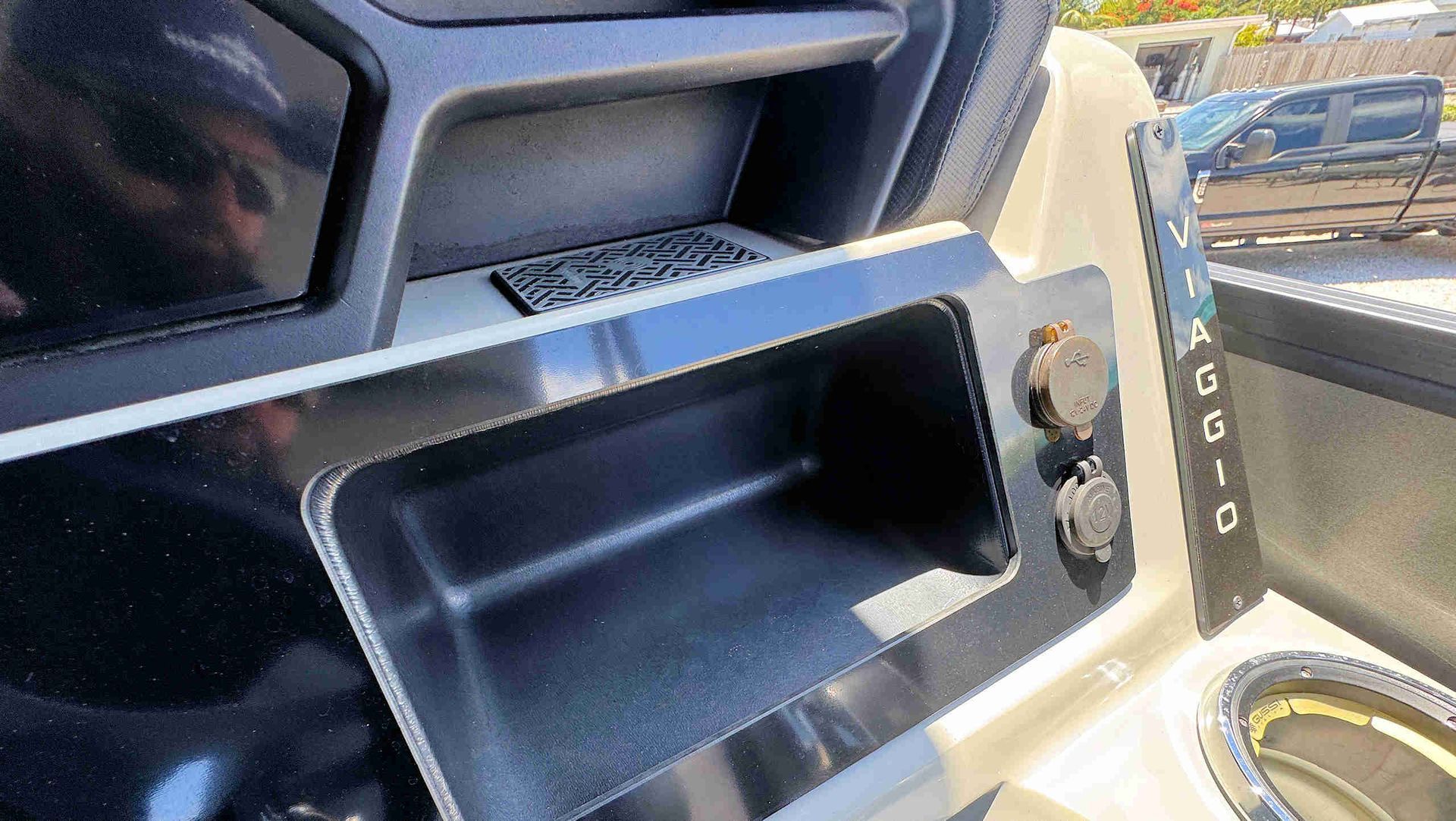 Tritoon helm with an open storage compartment and climate control knobs beside a cup holder.